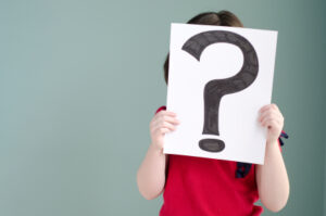 Girl holding sheet of paper with question mark drawn on it