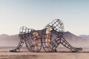 Two mesh figures sitting back to back with baby figures standing face to face inside them with a desert backdrop