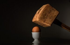 A wooden mallet held over a boiled egg sitting in an white china egg cup