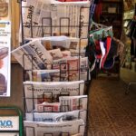 A full newspaper and magazine stand outside an open shop