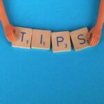 A pair of hands holding four wooden blocks in place which spell out the word 'tips' against a sky-blue surface