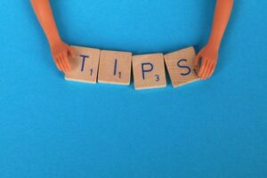 A pair of hands holding four wooden blocks in place which spell out the word 'tips' against a sky-blue surface