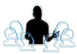 A silhouette of a person standing talking to a group of 6 represented by head outlines in a circle around the speaker