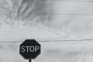 Black and white photo of a stop sign under a grey sky with overhead wires crossing