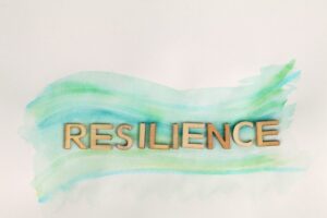 The word resilience made with wooden letters against a cream background with an abstract wave of green hues across it