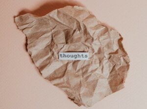 Crumpled brown paper with a typed piece of white paper with the word thoughts in the centre