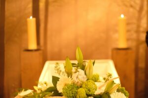 A white plate with a white and green flower arrangement and candles in the background